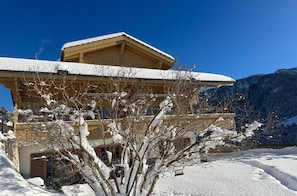 Un edificio de estilo chalet con techo cubierto de nieve y montañas al fondo.
