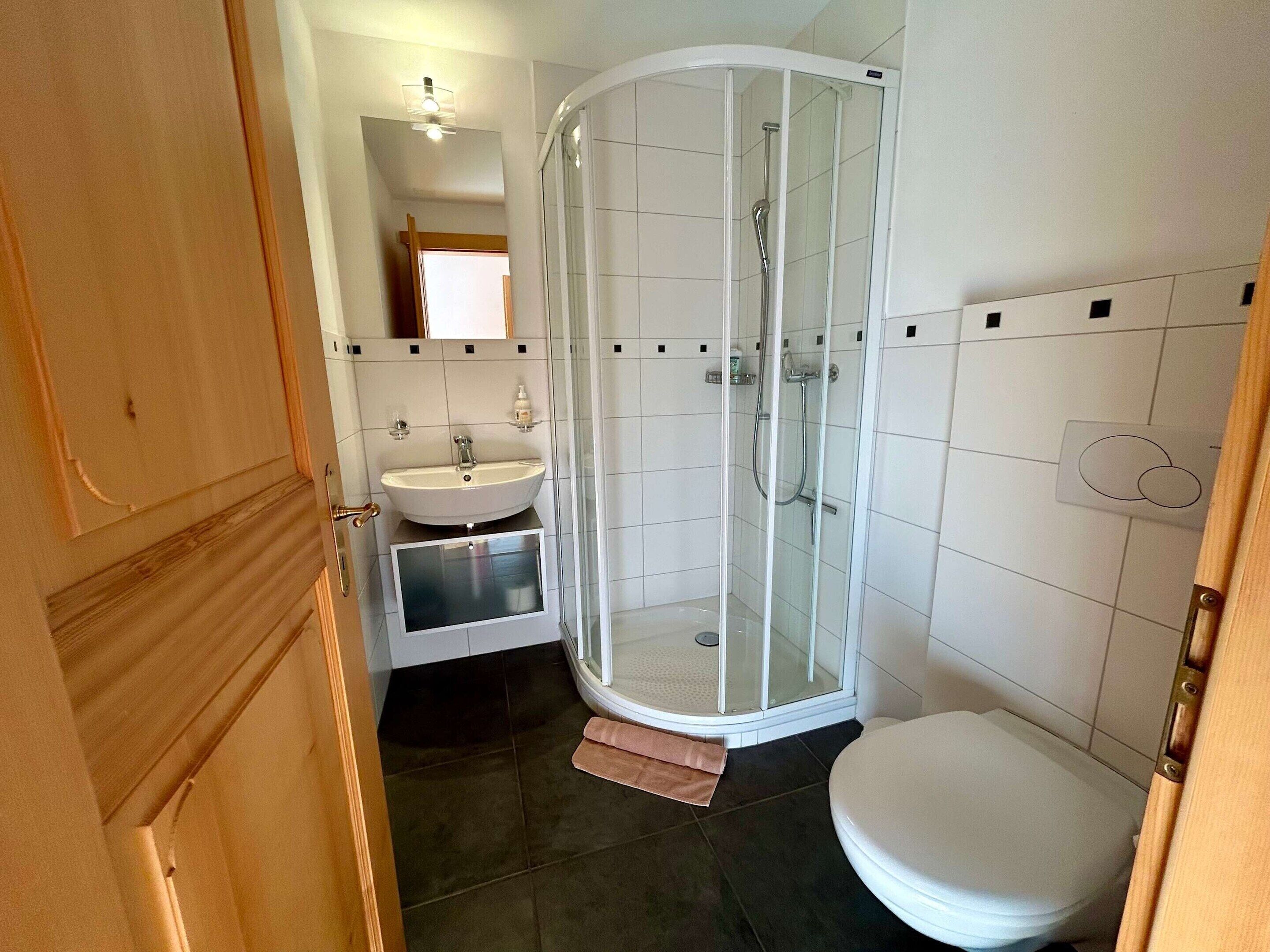 A bathroom with a glass-enclosed shower, a sink, and a toilet.