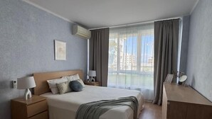 Une chambre d’hôtel moderne avec un grand lit, des tables de chevet avec des lampes, une commode et une vue sur les immeubles par la fenêtre.