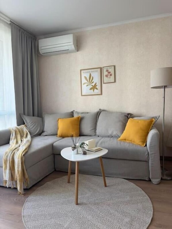 A modern living room with a grey sofa, two yellow cushions, a white coffee table, and a round rug.