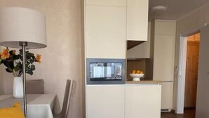 Un salon moderne avec un canapé, une table basse et une lampe. Il y a également un coin cuisine équipé de placards et d’un four à micro-ondes.