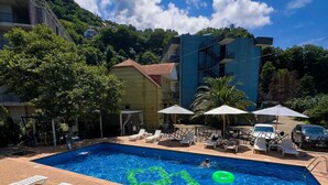 A swimming pool with lounge chairs and umbrellas, surrounded by buildings and trees. - Casa Del Mar (Batumi)