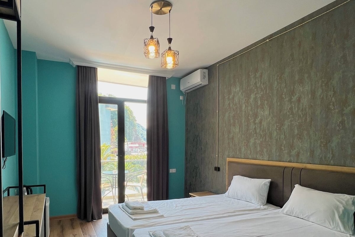 A hotel room with two beds, a desk, and a view of the outdoors.