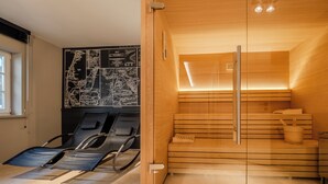Un cuarto de sauna con bancos de madera y una puerta de vidrio. Hay dos sillas de masaje con toallas. Un mapa está colgado en la pared.