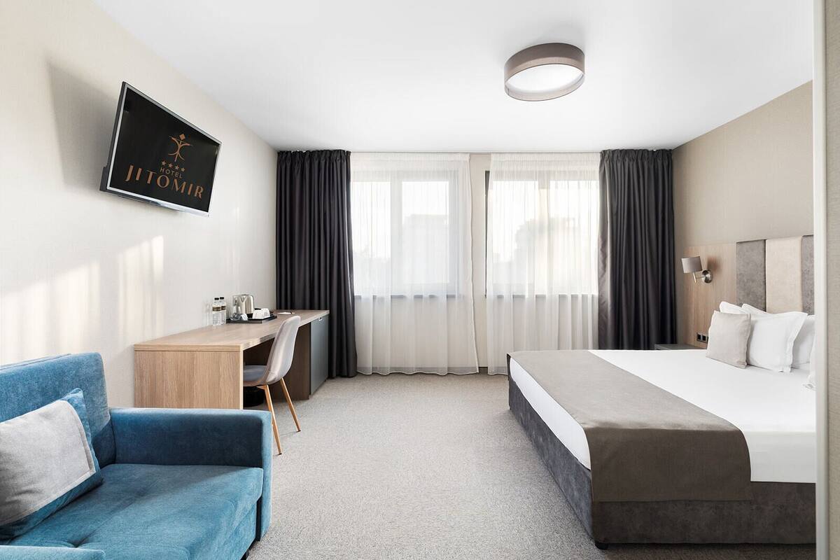 A hotel room with a bed, a desk, a chair, and a TV displaying the hotel name.