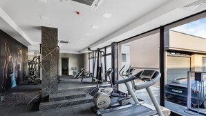 Un gimnasio moderno con diferentes equipos de ejercicio, un ventanal amplio y una estación de carga para vehículos eléctricos.