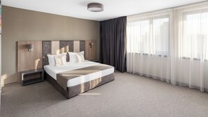 Habitación de hotel moderna con una cama grande, una mesita de noche, estante empotrado y un ventanal con cortinas translúcidas.