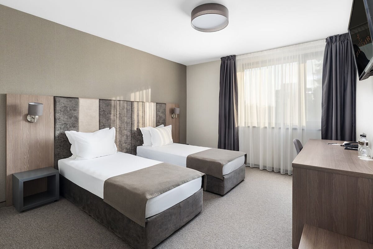 A hotel room with two beds, a desk, and a TV.