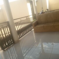 Varanda ampla com guarda-corrimão de metal preto, sofá bege e piso revestido que reflete a luz do sol.