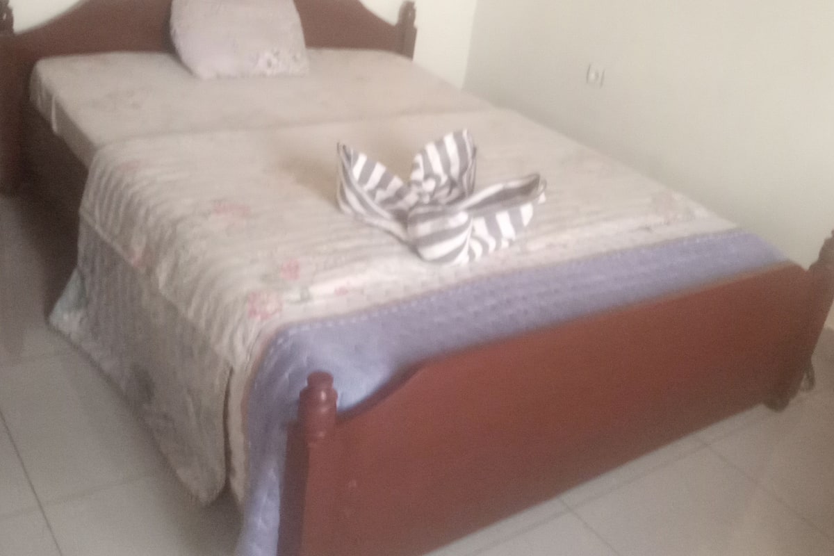 A bed with a wooden frame, a patterned bedspread, and a pair of striped slippers on it.