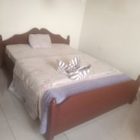 Uma cama com estrutura de madeira, uma colcha estampada e um par de chinelos listrados sobre ela.