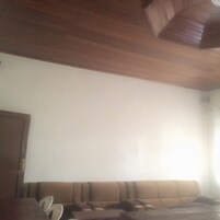 Uma sala de estar com sofá marrom, teto de madeira e parede branca.
