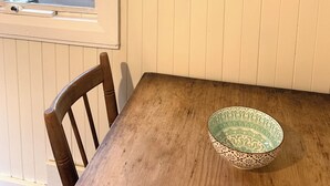 Ein Essbereich mit einem Holztisch, einem Stuhl, einer Schüssel, einem Fenster mit Jalousien und einem gerahmten Gemälde an der Wand.