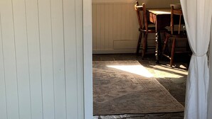 Ein Zimmer mit Steinboden, einem Holzespeisetisch mit Stühlen, einem Fenster mit Jalousien und einem Bild an der Wand.