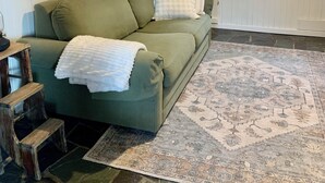 Ein grünes Sofa mit weißer Decke, ein gemustertes Teppich und eine hölzerne Bank.