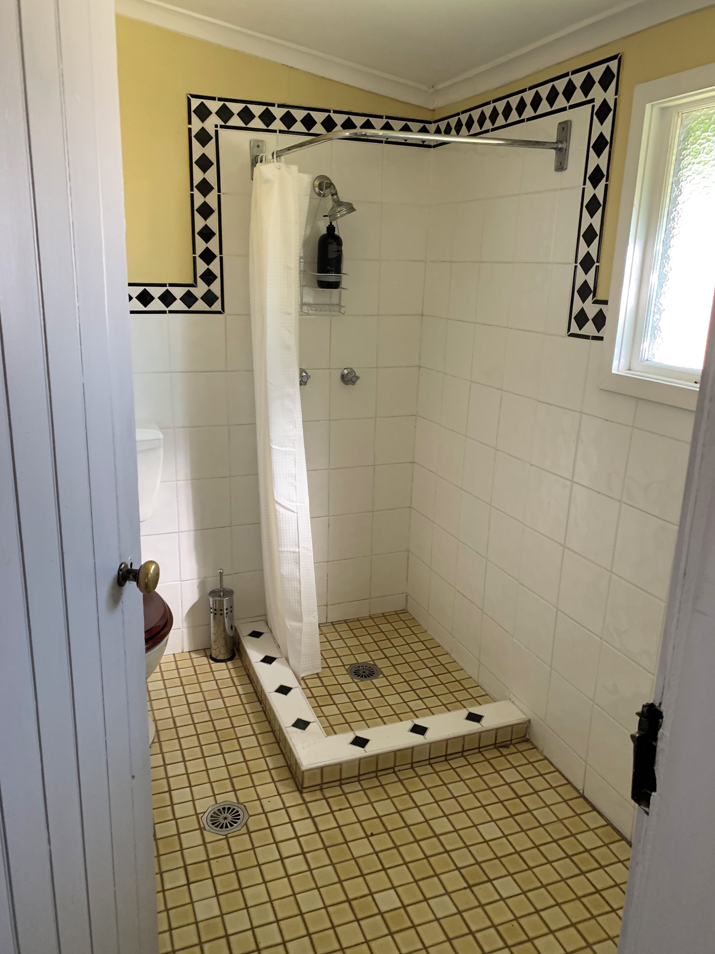 A small, tiled bathroom with a shower, a toilet, and a window.