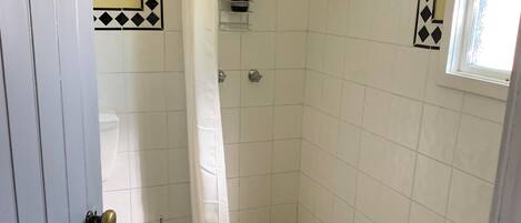 A small, tiled bathroom with a shower, a toilet, and a window.