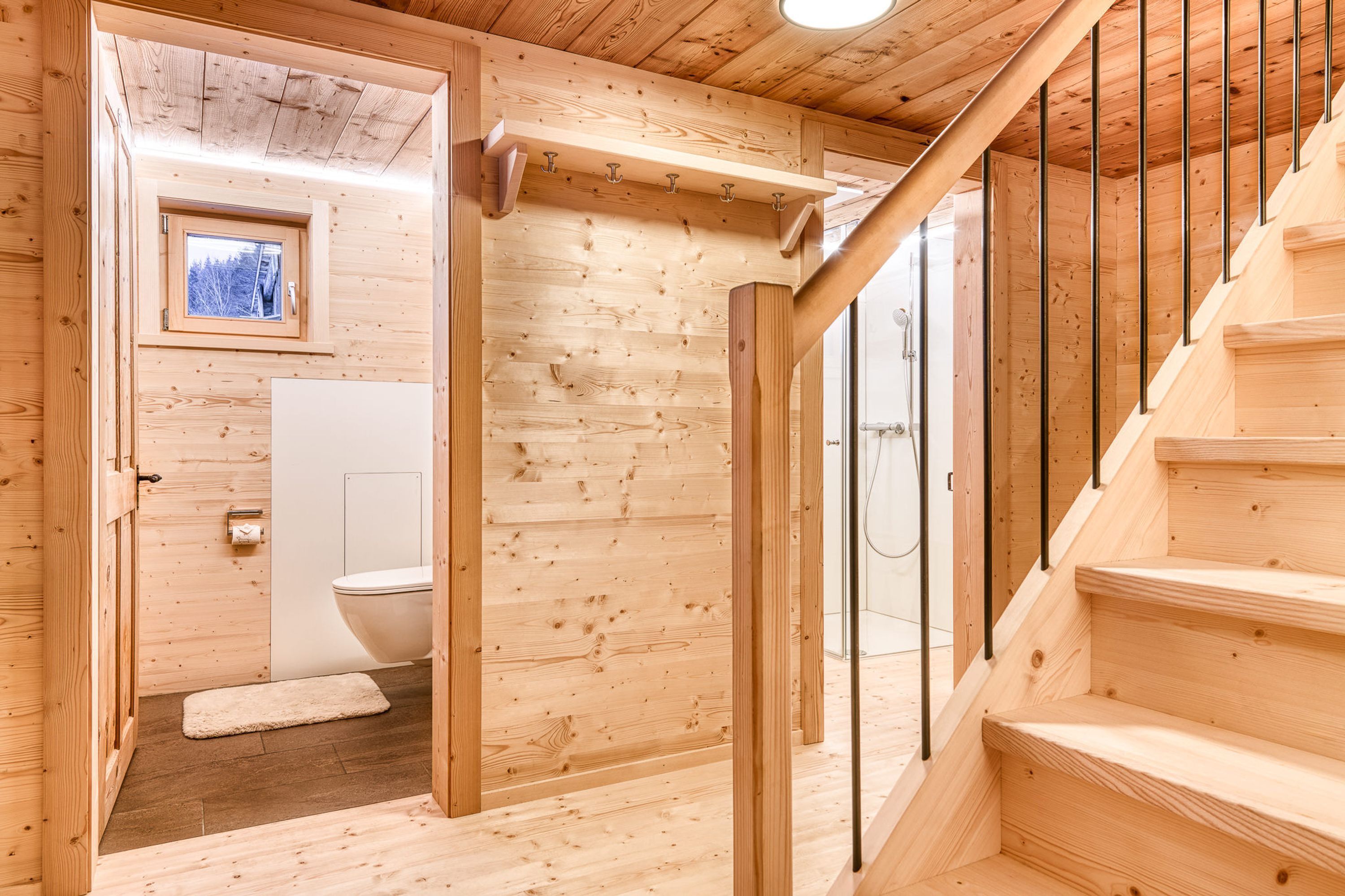 A wooden interior with a staircase, a window, and a toilet.