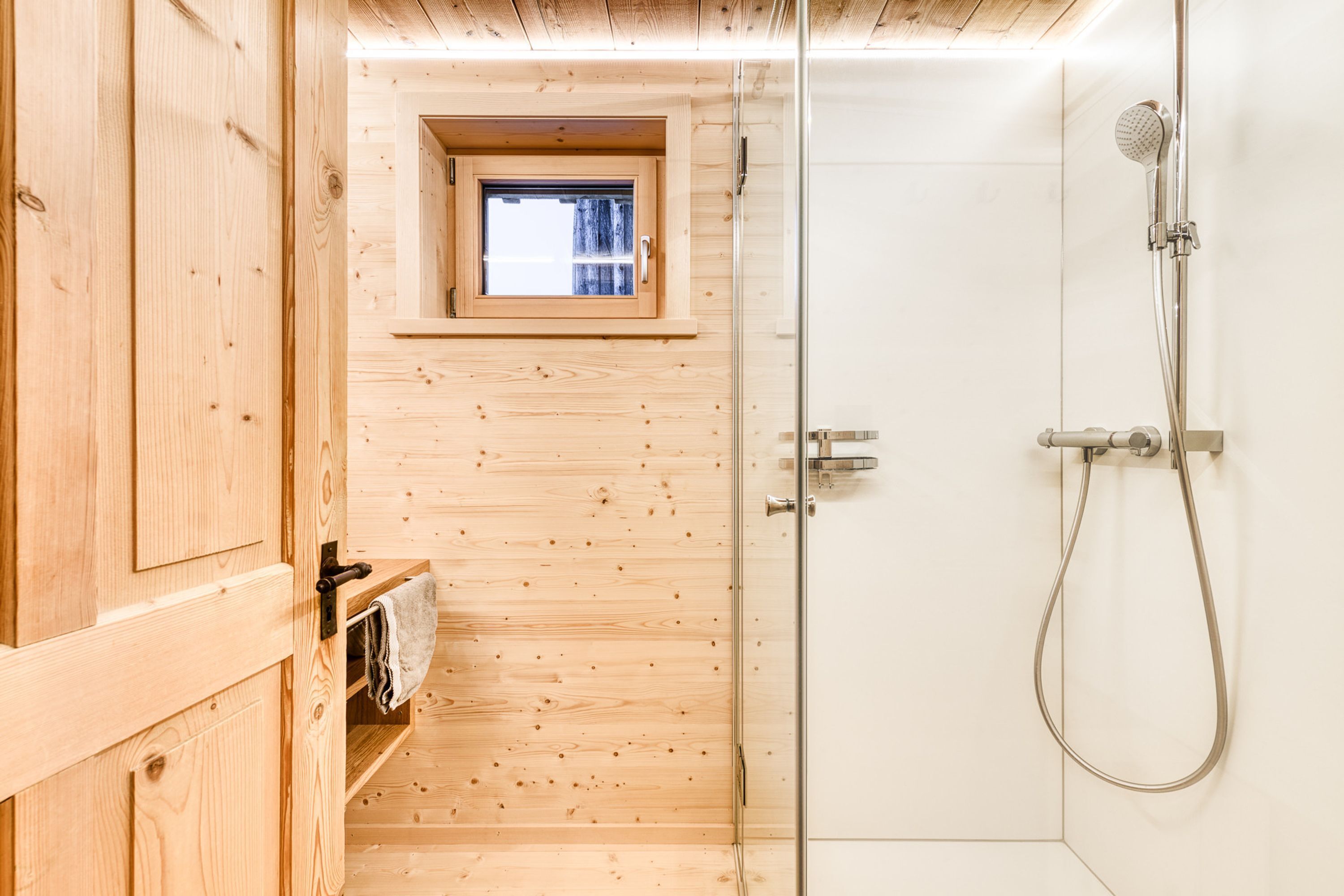 Un intérieur en bois avec une cabine de douche en verre, une petite fenêtre et un porte-serviettes.
