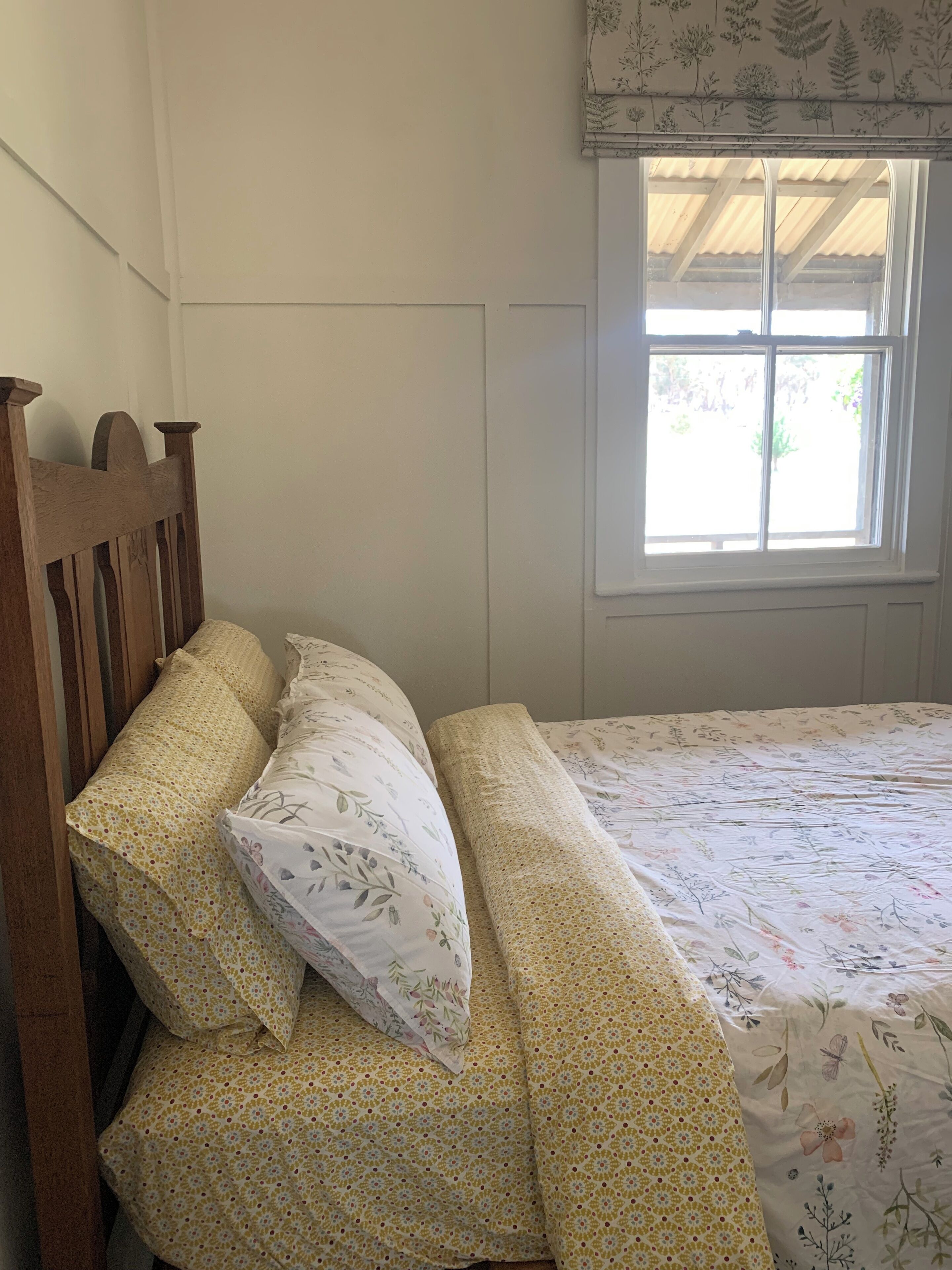 A bedroom with a wooden headboard, floral bedding, and a window with a view of greenery.