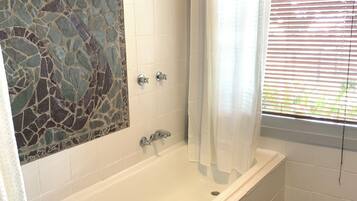A bathroom with a bathtub, shower, and a window with blinds.