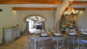 Un comedor con una mesa de madera rústica dispuesta para una comida, paredes de piedra y una araña.
