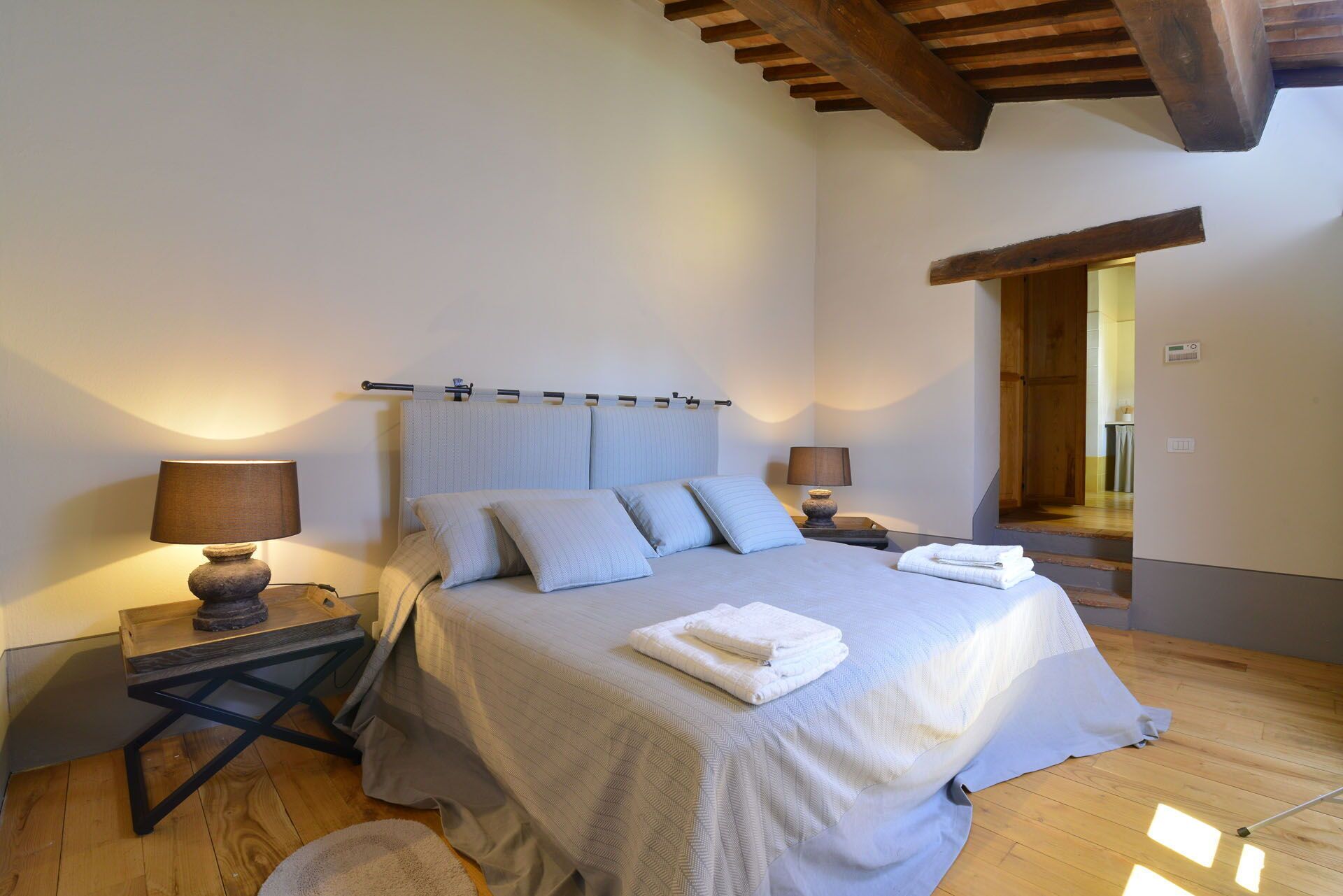 A bedroom with a bed, two bedside tables, a lamp on each table, and a wooden floor.