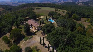 Vista aérea de una propiedad con piscina, rodeada de vegetación exuberante y colinas ondulantes al fondo.