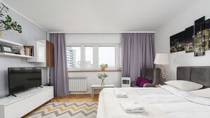 Ein modernes Hotelzimmer mit Bett, Fernseher, Schreibtisch, Stuhl und einem Vorhangfenster.