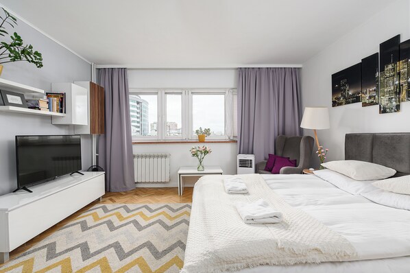 Ein modernes Hotelzimmer mit Bett, Fernseher, Schreibtisch, Stuhl und einem Vorhangfenster.