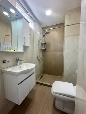 A modern bathroom with a white sink, mirror, and toilet. It includes a glass-enclosed shower area with a handheld showerhead and a handheld shower. - Nova Charm Aparthotel in Old Tbilisi (Tbilisi)