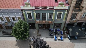 A multi-story building with a red roof, green and white facade, and a ground-level seating area with outdoor furniture. - Nova Charm Aparthotel in Old Tbilisi (Tbilisi)
