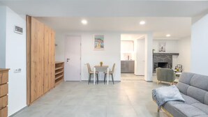 A modern living room with a grey sofa, a wooden wardrobe, a dining area with two chairs, and a kitchen in the background. - Nova Charm Aparthotel in Old Tbilisi (Tbilisi)