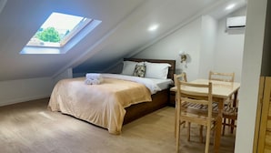 A bedroom with a skylight, a bed with a beige bedspread, a wooden nightstand, and a dining table with chairs. - Nova Charm Aparthotel in Old Tbilisi (Tbilisi)