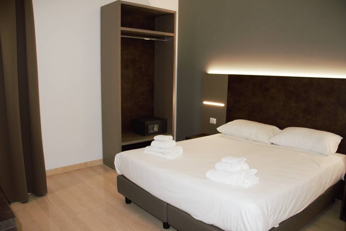 A hotel room with a bed, a wardrobe, and a bedside table with a lamp.