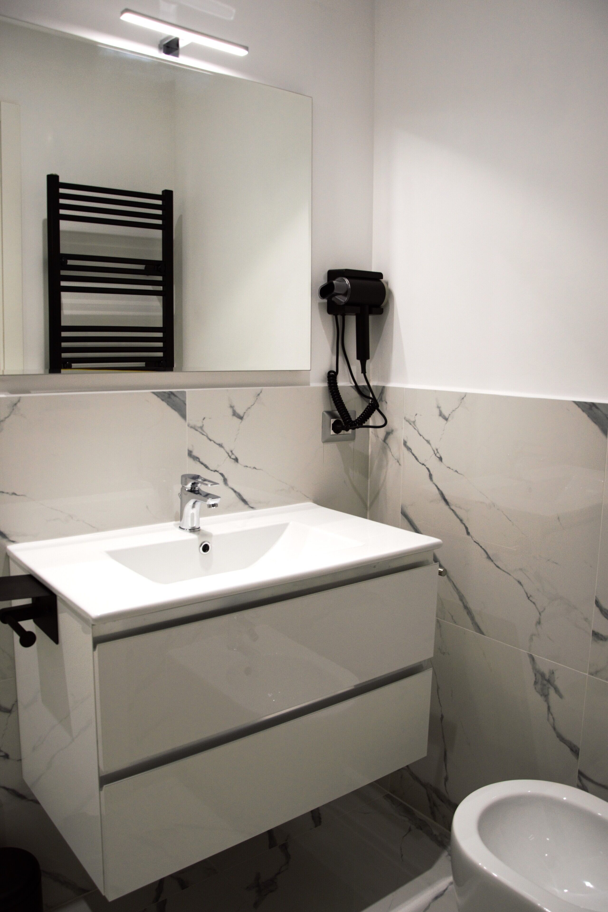 A modern bathroom with a white sink, a mirror, a towel rack, and a toilet.
