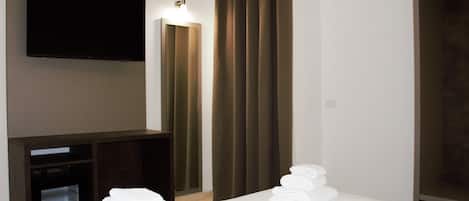 A hotel room with a bed, a flat-screen TV mounted on the wall, a wardrobe, and a set of towels on the bed.
