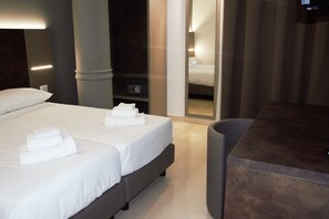 A modern hotel room with a large bed, a bedside table, and a mirror reflecting the room.