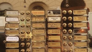 En ældgammel elevator med flere knapper, der er mærket med værelsesnavne og -numre.