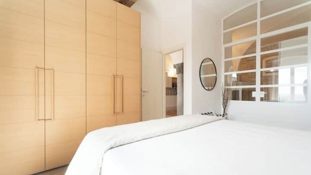 A bedroom with a large wardrobe, a bed with white bedding, and a mirror on the wall. - The Donizettino (Bergamo)