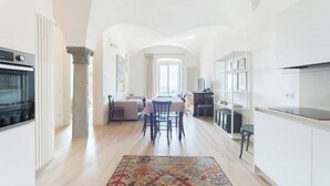 A spacious kitchen with white cabinetry, a dining area with a table and chairs, and a view through an arched doorway to a living area. - The Donizettino (Bergamo)