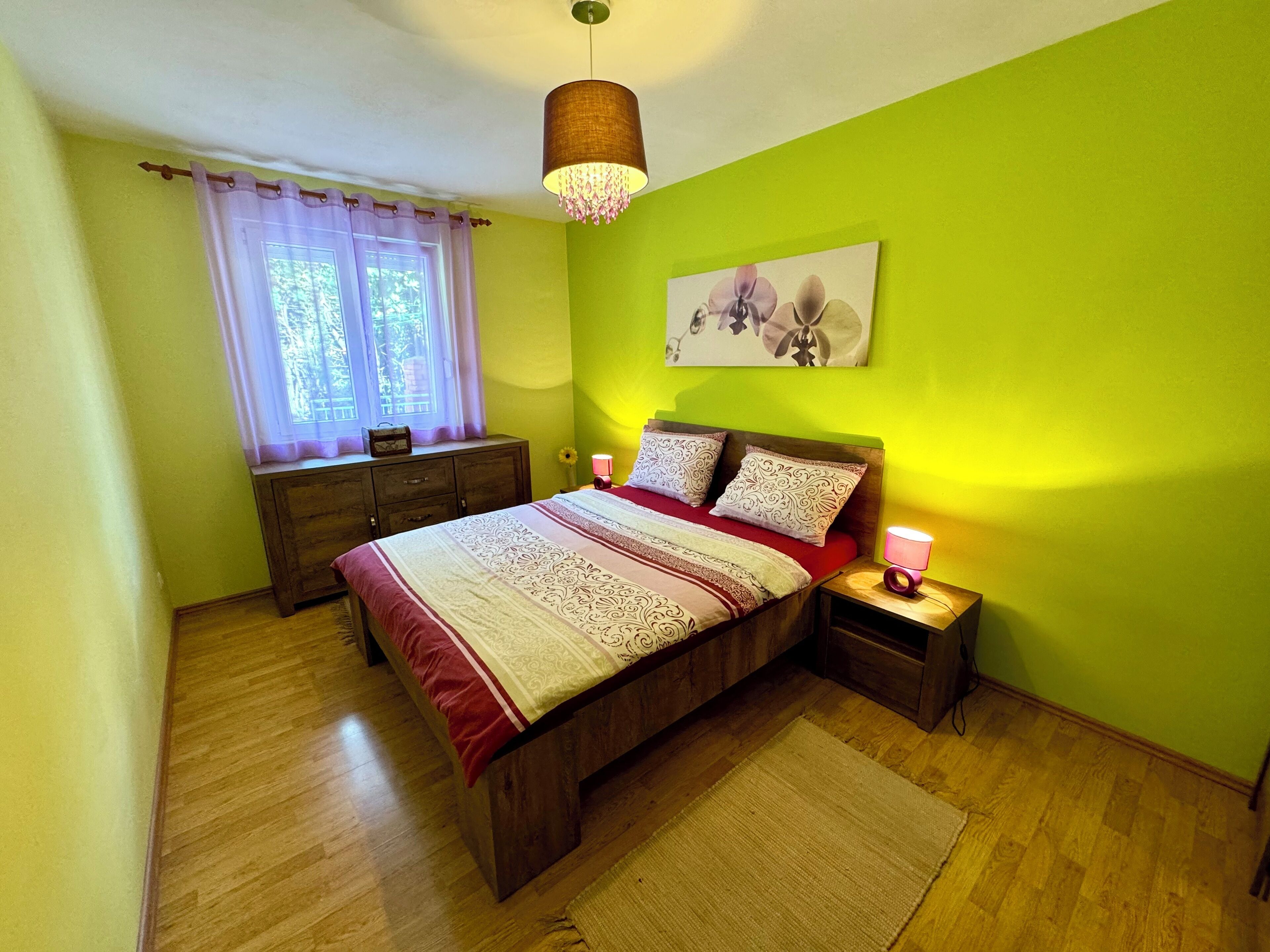 Une chambre à coucher avec un lit en bois, une table de chevet avec une lampe, une commode et une fenêtre avec des rideaux.