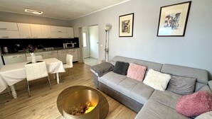 Ett modernt vardagsrum med en grå soffa, ett runt soffbord och en matplats med ett vitt bord och stolar.