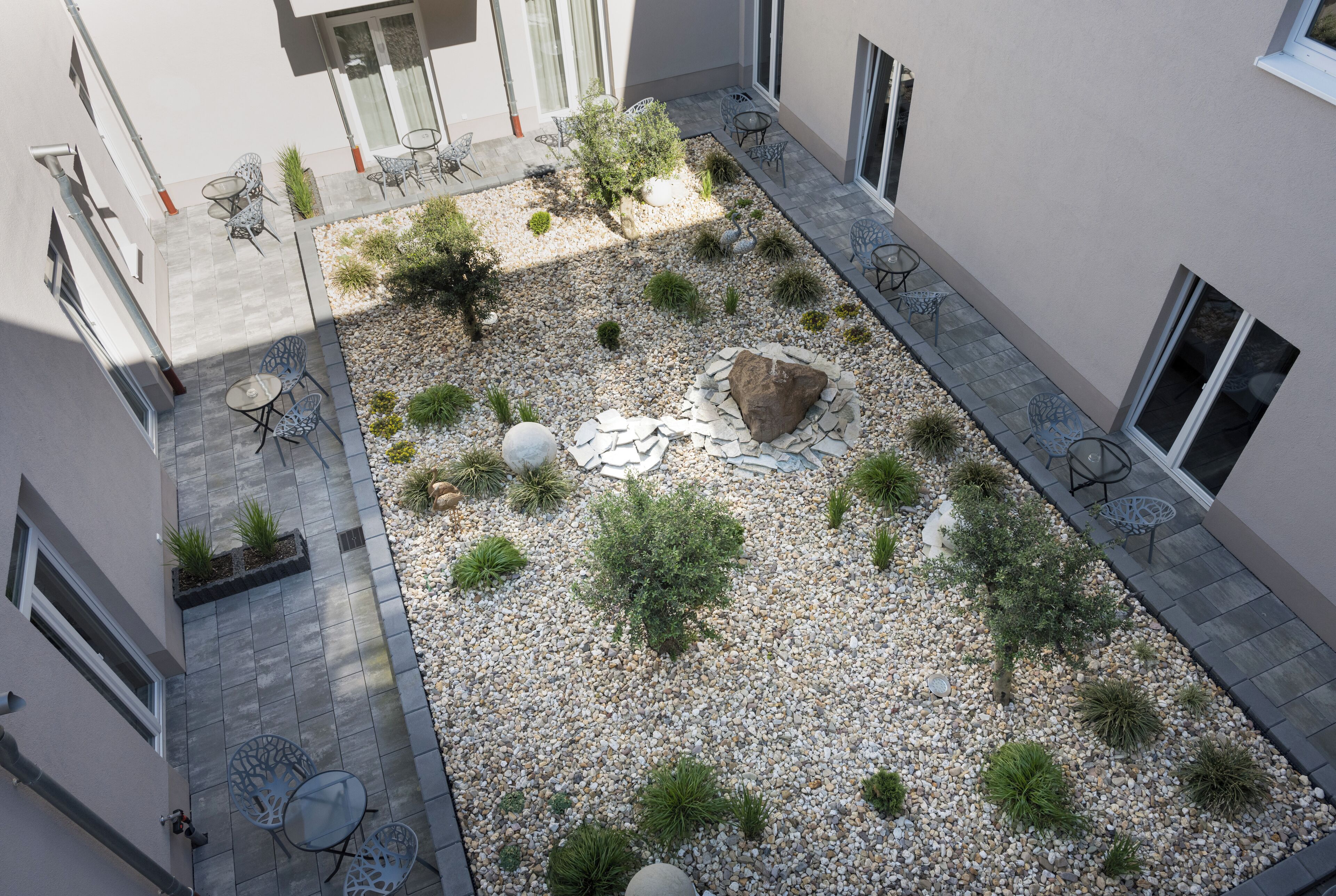 Un patio exterior con mobiliario, plantas y una roca central.