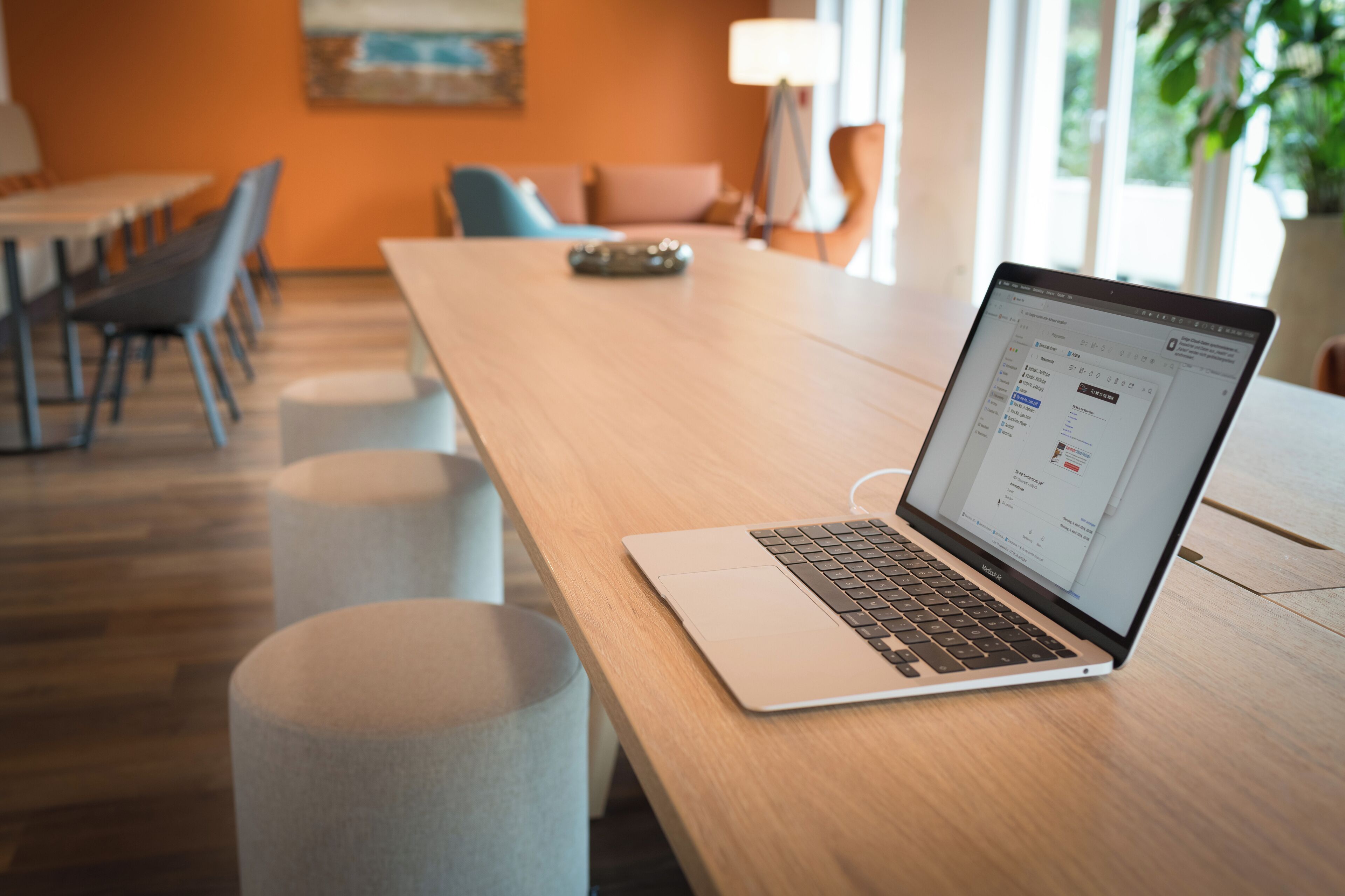 Una laptop sobre una mesa de madera en una habitación de diseño moderno, con un sofá, sillas y una lámpara.