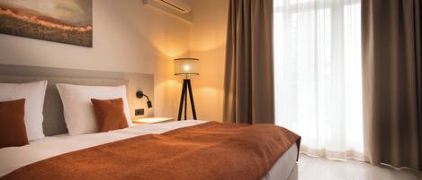 Een hotelkamer met een groot bed, een bedlamp, een wandairconditioner en een raam met gordijnen.