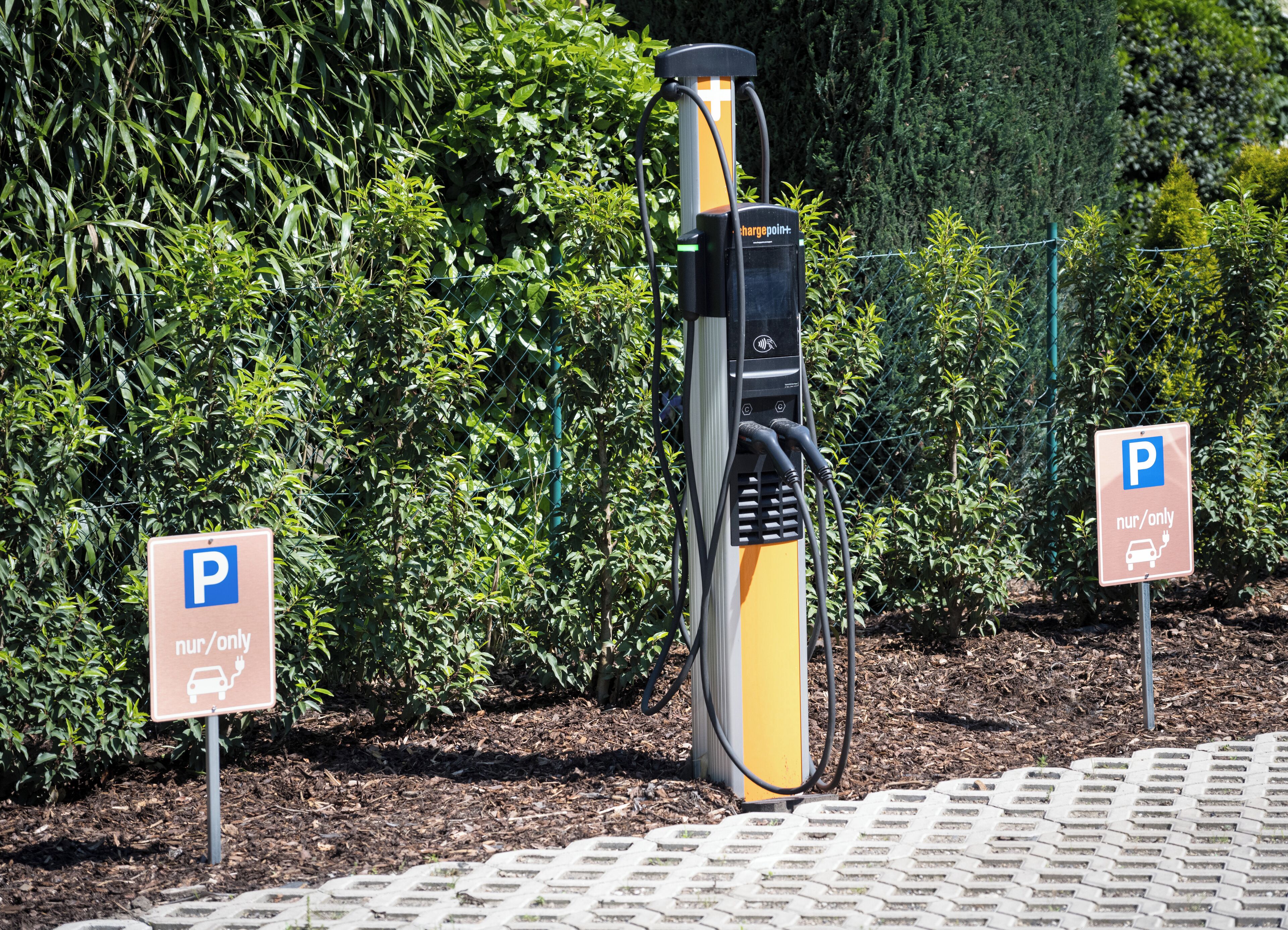 Un espace de stationnement équipé de bornes de recharge pour véhicules électriques et d’un panneau indiquant qu’il est réservé aux personnes accompagnées d’un enfant en bas âge (« pour les personnes avec enfants en bas âge uniquement »).
