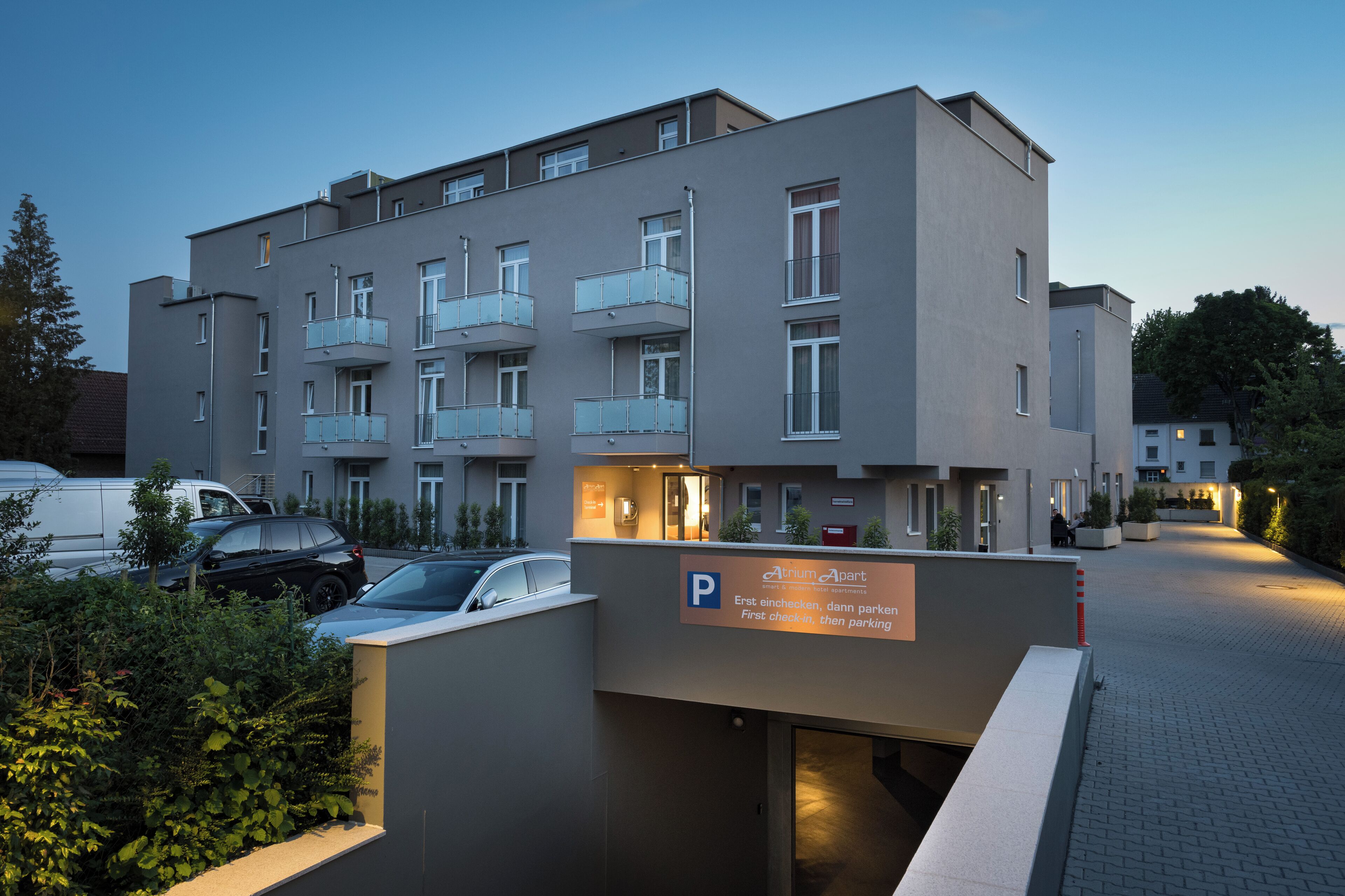 A modern apartment building with a parking entrance, multiple balconies, and a sign indicating parking rules.