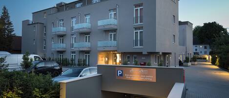 A modern apartment building with a parking entrance, multiple balconies, and a sign indicating parking rules.