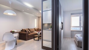 Egy modern nappali, amelyben kanapé, dohányasztal és egy étkező található. Egy nyitott ajtón keresztül a konyha is belátható.